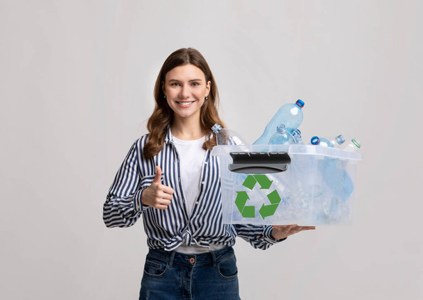 Hulladékválogatás. Mosolygó fiatal nő hordozó tartály műanyag palackok újrahasznosítására - Fotó, kép