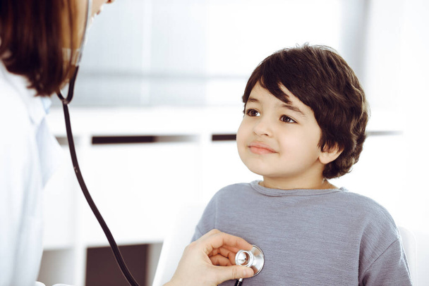 Doctor-woman examining a child patient by stethoscope. Cute arab boy at physician appointment. Medicine concept - Foto, Bild