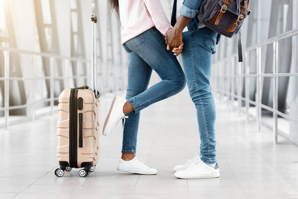 Обрезанный снимок черной пары держась за руки, стоя в терминале аэропорта - Фото, изображение