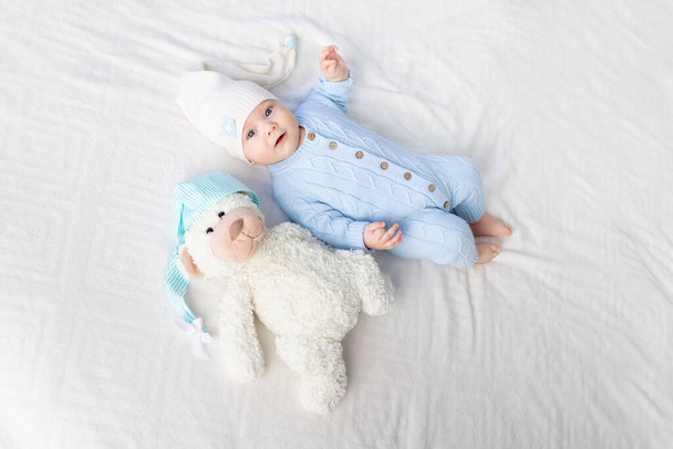 bebê feliz na cama em um capuz. Têxteis e roupa de cama para crianças. Bebê recém-nascido com um urso de brinquedo - Foto, Imagem
