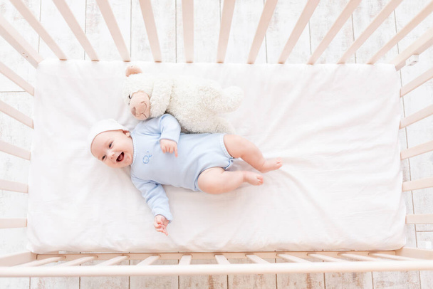 baby in crib with teddy bear toy goes to bed or woke up in the morning, family and birth concept - Fotó, kép