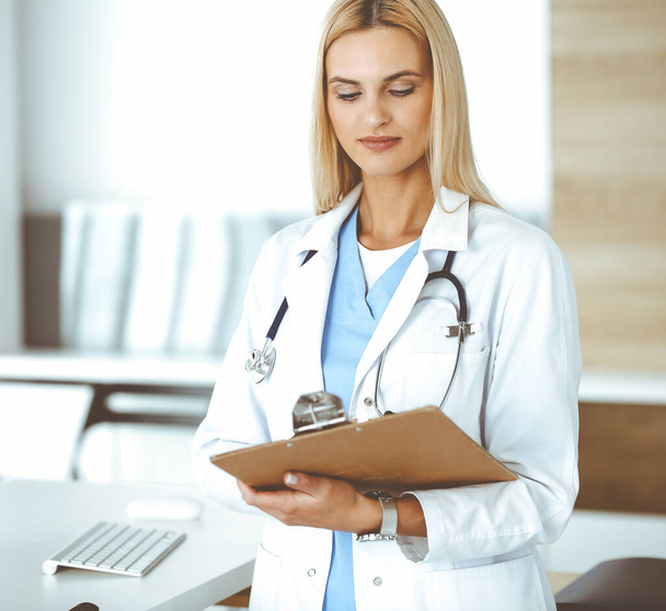 Doctor woman at work in hospital controls medication history records and exam results while using clipboard. Medicine and healthcare concept - Foto, Bild