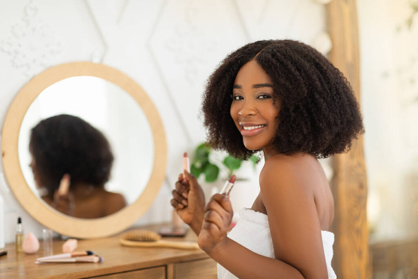 Cheerful young black lady applying lipstick in front of mirror at home, copy space - Foto, Imagen