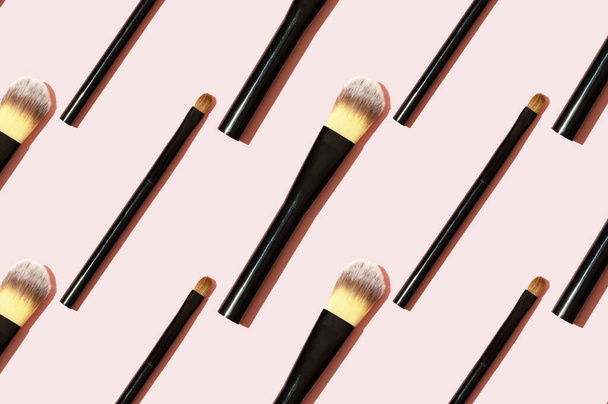 A pattern of black makeup brushes. Modern bright decorative background. Women's accessories on a pink background. Professional makeup artist's tool for applying eyeshadow and foundation. - Photo, Image