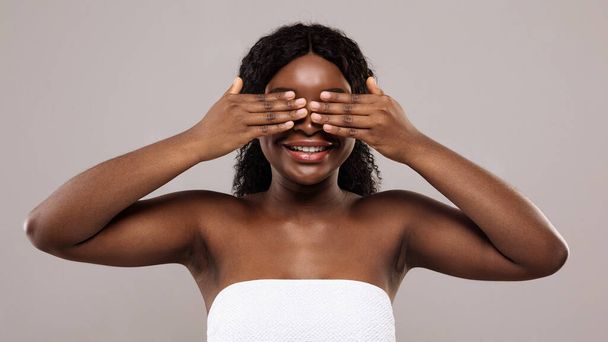 Бодрая чёрная женщина с полотенцем, закрывающим глаза обеими руками - Фото, изображение