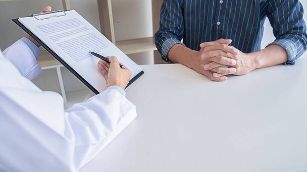 Patient listening intently to a male doctor explaining patient symptoms or asking a question as they discuss paperwork together in a consultation - Foto, Imagen