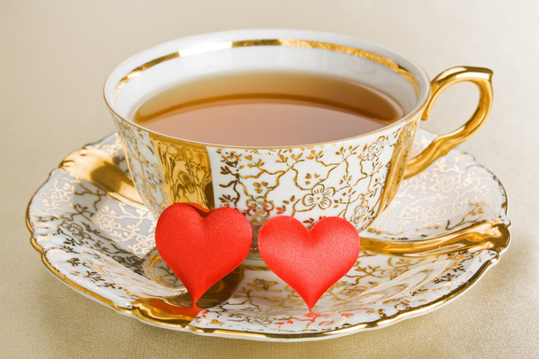 Chá de xícara de ouro antigo com dois corações vermelhos
 - Foto, Imagem
