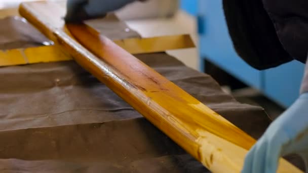 Zpracování dřevěné desky s lakem. Tesař v rukavicích malovat dřevěný povrch s hnědým lakem - Záběry, video