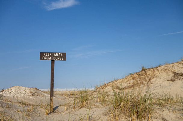 Tahta kahverengi ve beyaz plaj T işareti. Üzerinde "Kumullardan uzak durun" yazan kelimeler var. - Fotoğraf, Görsel