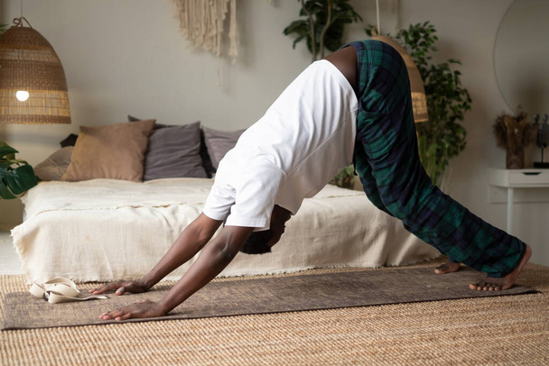 Young african man working out, standing in yoga downward facing dog pose, adho mukha svanasana - Photo, Image