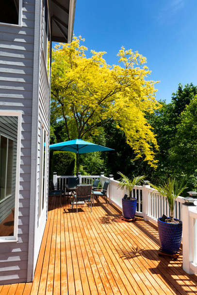Vista vertical de la cubierta de cedro de madera exterior del hogar con árboles en color estacional completo junto con muebles y plantas de palmeras  - Foto, imagen