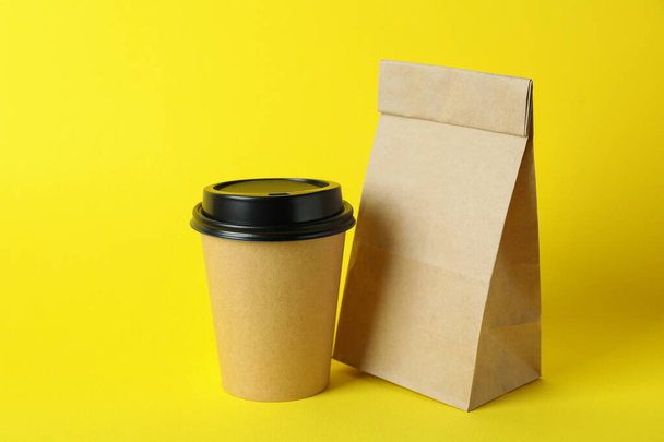Χάρτινη κούπα και χάρτινη σακούλα σε κίτρινο φόντο - Φωτογραφία, εικόνα