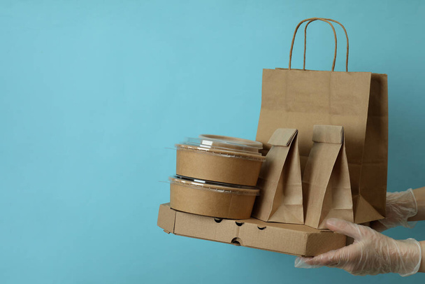 Mani in guanti tenere i contenitori di consegna per il cibo da asporto su sfondo blu - Foto, immagini