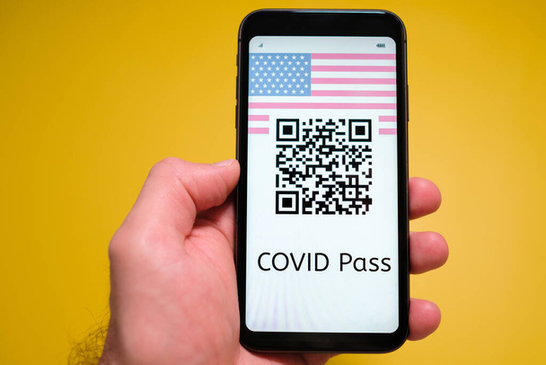 黄色の背景に男性の手でスマートフォンの画面上に米国のフラグとQRコードでCovidのパス, 5月2021,サンフランシスコ,米国. - 写真・画像