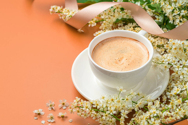 Cappuccino šálek detailní záběr na terakotové pozadí s květinami a stuhou. Boční pohled, kopírovací prostor. - Fotografie, Obrázek