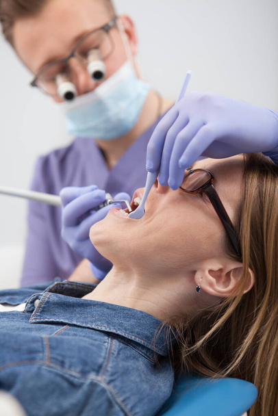 Κάθετη περικοπή κοντά σε μια γυναίκα ασθενή που έχει οδοντιατρική εξέταση σε οδοντιατρική κλινική - Φωτογραφία, εικόνα