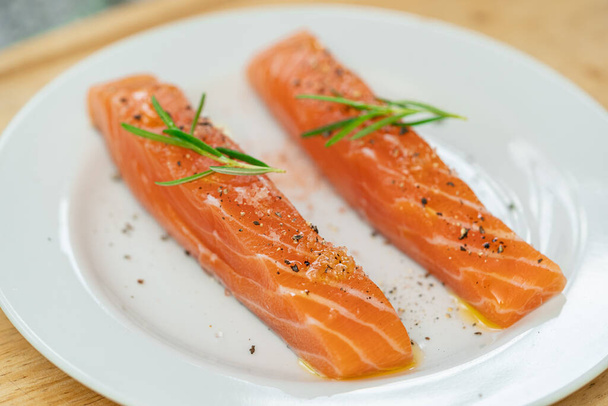 Salmon steak a piece of fresh home cooking with rosemary, olive oil, black pepper and himalayan salt on a white plate. Focus select and blur close up and Macro photography. - Фото, зображення
