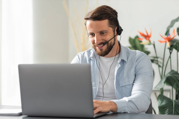 Happy caucasian man customer service worker communicates with the client using a headset with a microphone, call center employee, advises clients online, support operator - Foto, Bild