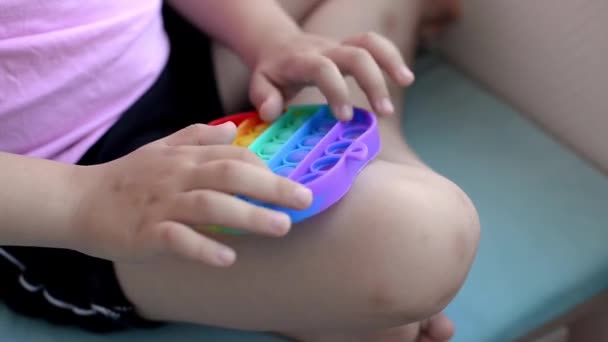Девушка в розовой футболке играет с модной игрушкой. красочные антистрессовые сенсорные игрушки Фиджет толкать поп его в руках ребенка, может быть использован для тренировки с аутистами - Кадры, видео