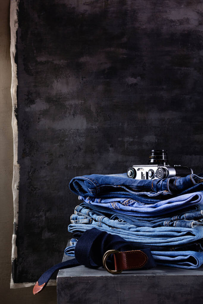 Denim jeans and leather belt at old grey cube near grey wall background.  Stack of jeans fashion at abstract surface - Photo, Image