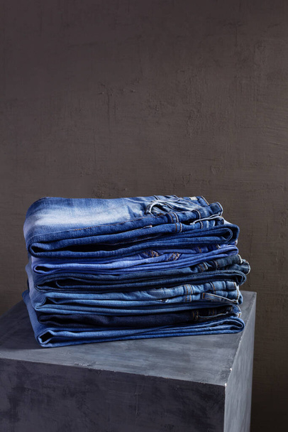 Denim jeans at old grey cube near grey wall background texture.  Stack of jeans fashion at abstract surface - Photo, Image