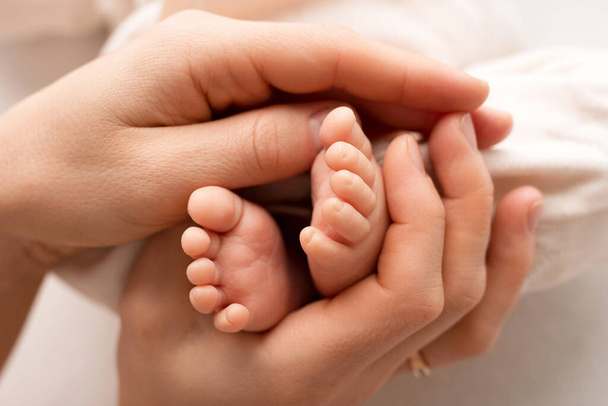 Μικρά πόδια ενός νεογέννητου παιδιού στα χέρια ενός γονέα. Ένα μωρό μιας εβδομάδας. Η εικόνα των πρώτων ημερών της ζωής. Αντίληψη εικόνα της ευτυχισμένης οικογένειας, μητρότητα και ευτυχισμένη παιδική ηλικία. - Φωτογραφία, εικόνα