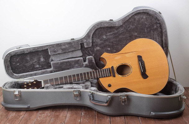 Musical instrument - Broken acoustic guitar in hard case on a white wall background and wooden floor. - Photo, Image