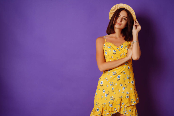 Smiling woman in yellow dress and hat posing purple background. Fashion, style, summer concept.  - Fotó, kép