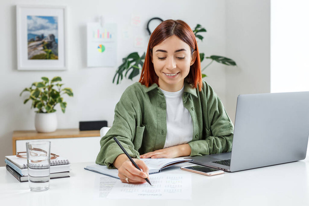 Woman remotely working at home with laptop computer. Young businesswoman planning her time. Concept of online business, freelance, home office and telework for entrepreneur. - 写真・画像