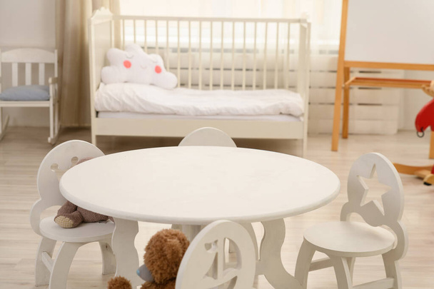 a white round table for children stands against the background of the children's room. nearby there are white children's chairs. - Fotografie, Obrázek