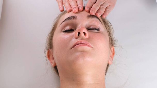 Massaggio viso trattamento di bellezza. Primo piano di una giovane donna faccia sdraiata sulla schiena, ottenere massaggio lifting facciale, pizzicare e rotolare tecnica - Foto, immagini