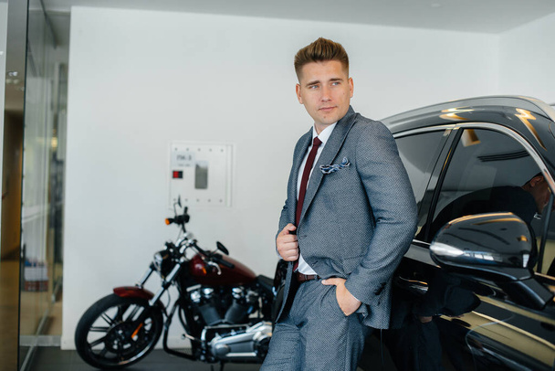A young businessman looks at a new car in a car dealership. Buying a car - 写真・画像