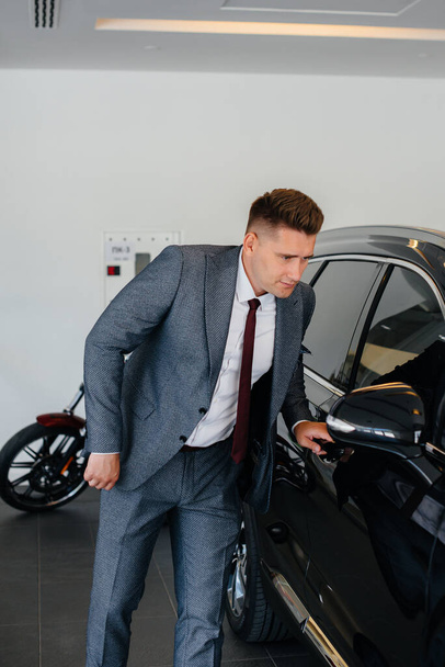 A young businessman looks at a new car in a car dealership. Buying a car - Фото, изображение