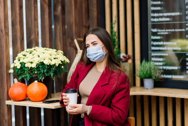 Restoranda yüz maskesi takan genç bir kadın, koronavirüs salgınını korumak için yeni normal bir konsept. - Fotoğraf, Görsel