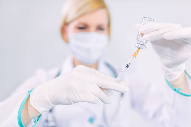 Zbliżenie lekarza w masce ochronnej i rękawiczkach trzymającego strzykawkę i probówkę ze szczepionką gotową do użycia podczas pandemii wywołanej przez kovid-19 w klinice kliniki kliniki badania laboratoryjne - Zdjęcie, obraz