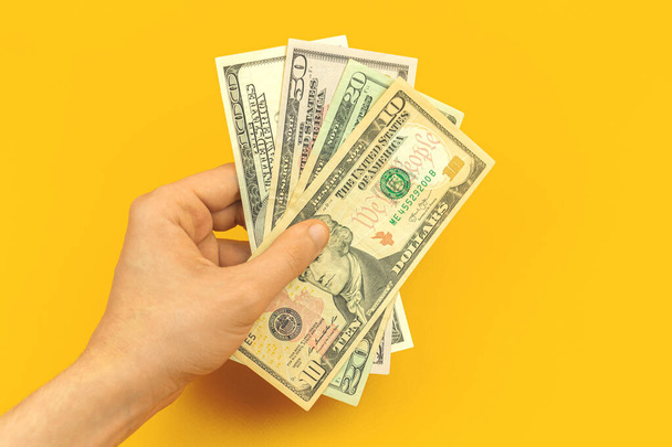 Чоловік тримає в руках свою зарплату, гроші, різні доларові купюри на жовтому фоні фото
 - Фото, зображення