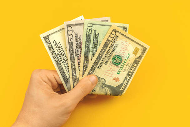 Férfi a fizetését a kezében, számolás és bemutatása fizetés koncepció, sárga háttér és irodai asztal - Fotó, kép