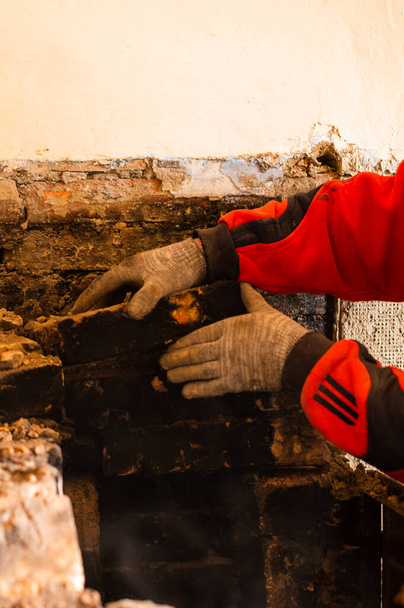 El hombre destruye una vieja estufa de ladrillo, ladrillo negro en hollín, desmantelando la vieja superficie de la cocina. nuevo - Foto, Imagen