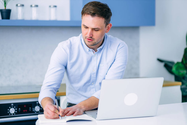 Jeune homme d'affaires concentré prenant des notes pendant un processus de travail. Travailleur indépendant employé au moyen d'un ordinateur. - Photo, image
