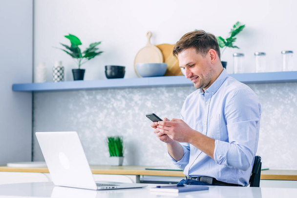 Profesjonalny mężczyzna trzymający nowoczesny smartfon, piszący na maszynie, przewijający się po ekranie i przeglądający, myślący o sprawach służbowych, piszący SMS-y w biurze za pomocą aplikacji mobilnej. - Zdjęcie, obraz