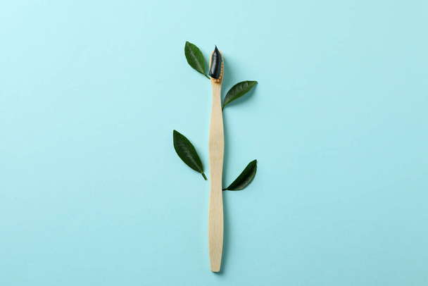 Eco friendly toothbrush with toothpaste and leaves on blue background - Fotoğraf, Görsel