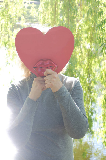 La chica envía un beso de aire con grandes labios decorativos rojos con un corazón de papel. Día Mundial del Beso. - Foto, imagen