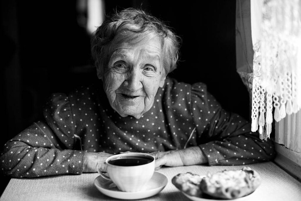 Egy idős nő teát iszik a házában. Fekete-fehér portré. - Fotó, kép