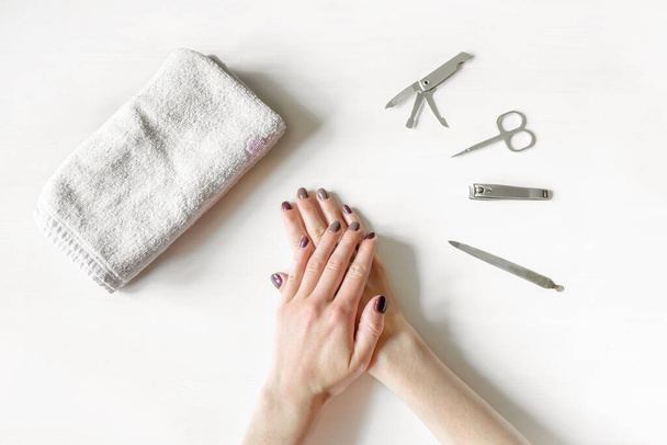 Close-up van de vrouw handen met gepolijste nagels en manicure instrumenten. Jonge blanke vrouw ontvangt Franse manicure thuis of in de nagelsalon. manicure, zelfverzorging, schoonheidsbehandelingen zelf - Foto, afbeelding