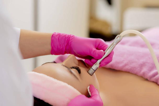 The cosmetologist makes the procedure Microdermabrasion of the facial skin of a beautiful, young woman in a beauty salon.Cosmetology and professional skin care - Foto, afbeelding