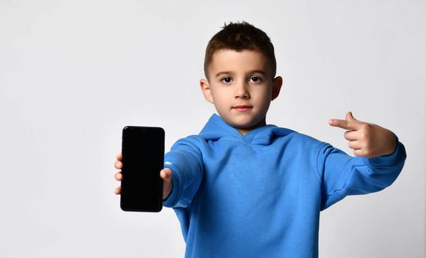 Close up portrait of a little boy holding a mobile phone and pointing his finger at it. - Фото, зображення