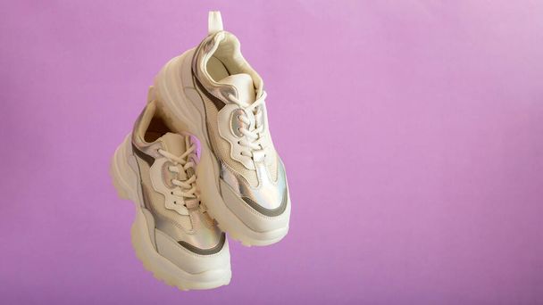 White sneakers fly on purple wall. Female white leather shoes on purple background. Pair of stylish urban sneakers. Comfortable sportswear hipster womens shoes. Long web banner with copy space - Foto, imagen