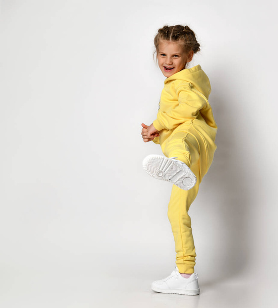 Little girl in a fashionable yellow sports suit and white sneakers on a white background. - Фото, зображення