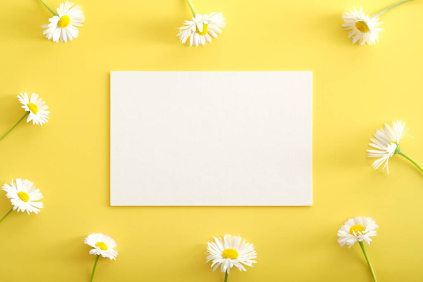 Chamomiles flowers and white paper card mockup on yellow background. Happy Mother's Day, Women's Day, birthday greeting card template. - Fotoğraf, Görsel