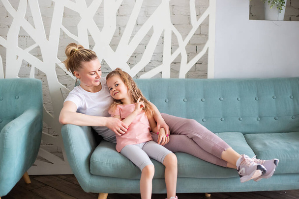 Little caucasian girl sitting together with mother on sitting on the sofa in living room, hugging and kissing each other. Spending time with children at home. - Foto, immagini